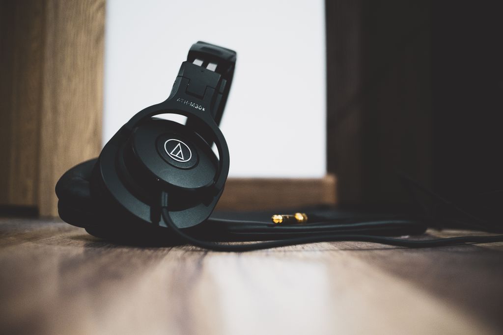 Stylish black headphones with cable lying on a wooden floor in a low-angle shot.